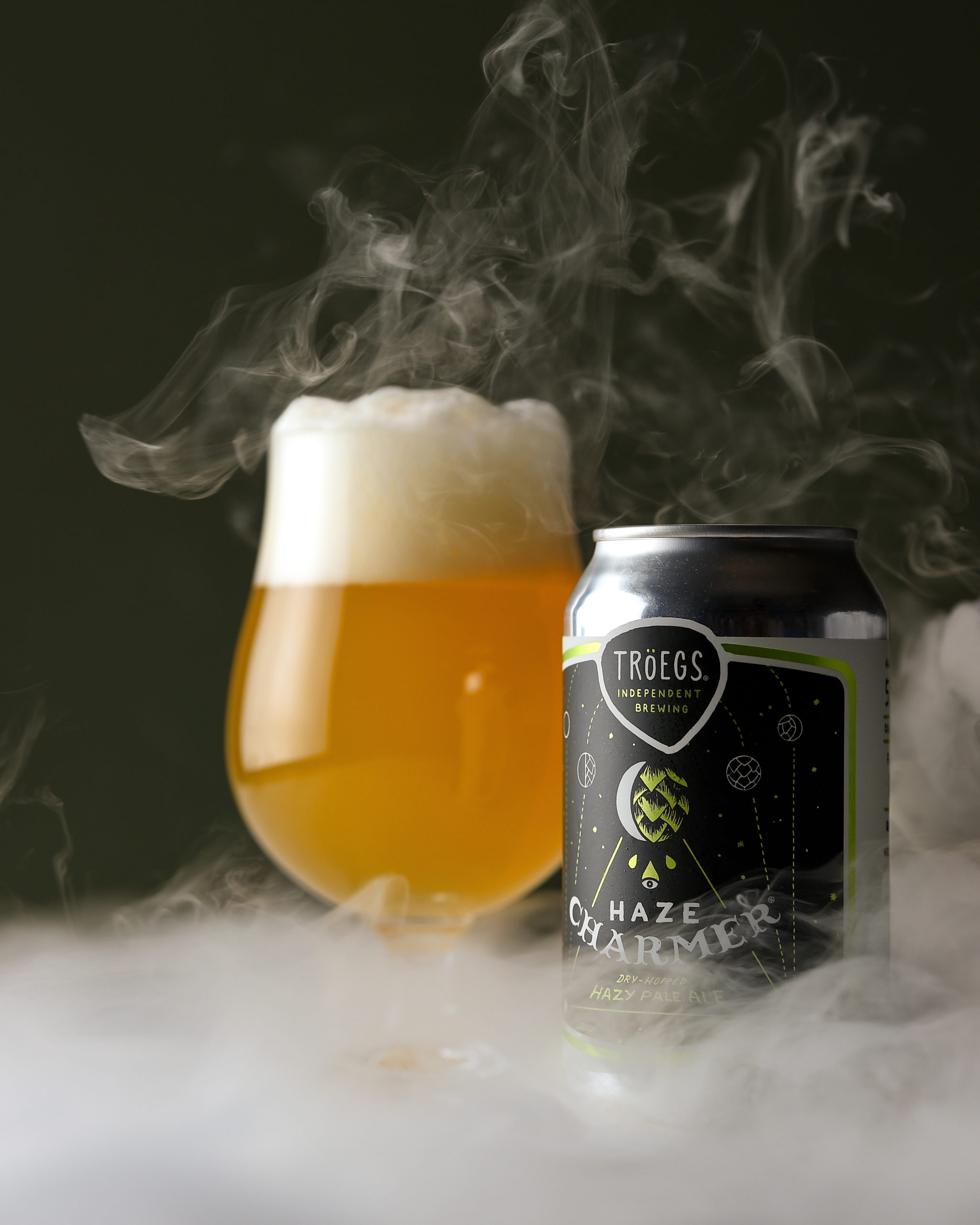 Haze Charmer can and poured glass of the hazy IPA, with mist in the foreground and background.