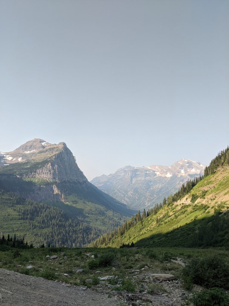Mountains, glaciers visible near some of the peaks, tree-covered slopes. View partway up Going to the Sun Road in Glacier National Park.