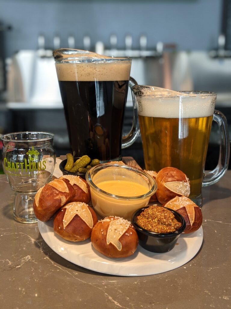 Pitchers of beer next to plate of pretzel buns, cheese dip and stone-ground mustard.