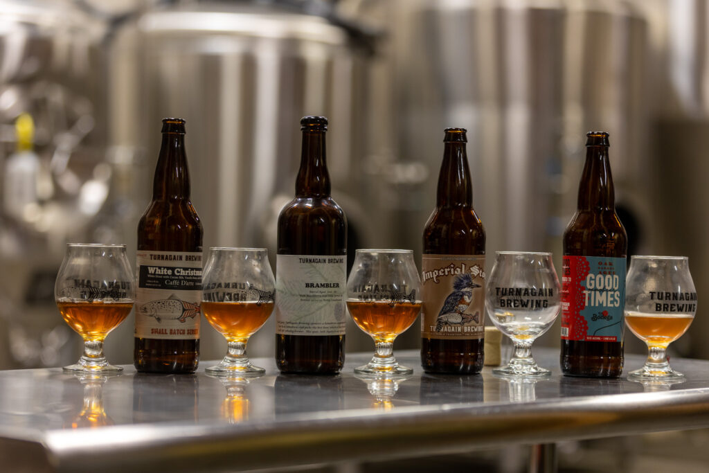 White Christmas white stout, Brambler, Imperial Stout, and Good Times bottles, lined up with beer glasses in between.