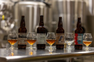 White Christmas white stout, Brambler, Imperial Stout, and Good Times bottles, lined up with beer glasses in between.