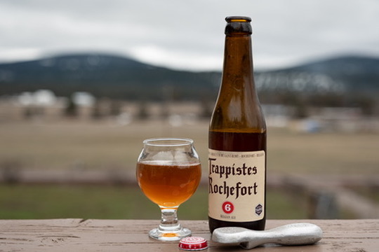 Bottle of Rochefort 6 ale next to a bottle opener and the cap from the bottle, with a small tasting glass of the same beer.