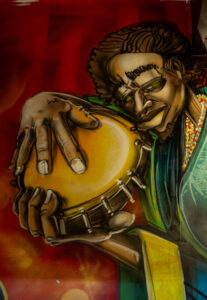 Mural of a man playing a pandero hand drum. The mural is on the wall above the door of Cervecería del Callejón.