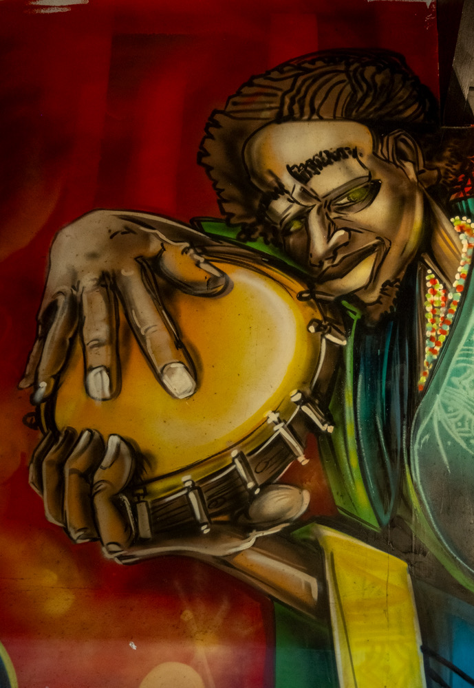 Mural of a man playing a pandero hand drum. The mural is on the wall above the door of Cervecería del Callejón.