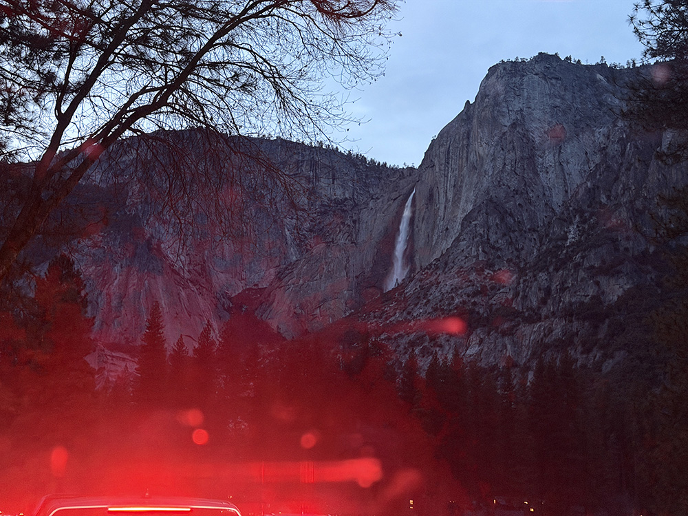 Red haze from car taillights in the foreground, with Horsetail Falls in the background.