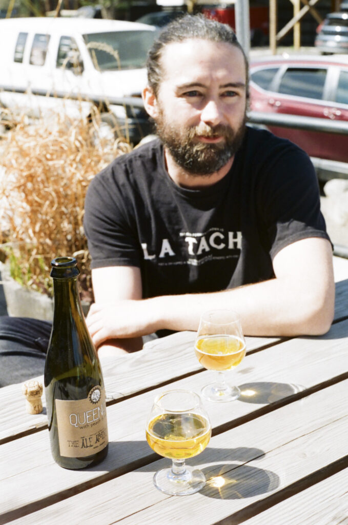 Connor Currie with a bottle of Queen of Noise, on the back porch of The Ale Apothecary, Bend location, April 18th, 2026.
