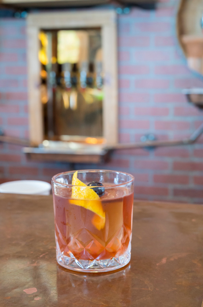Rum old-fashioned cocktail in a rocks glass, on a copper bar.
